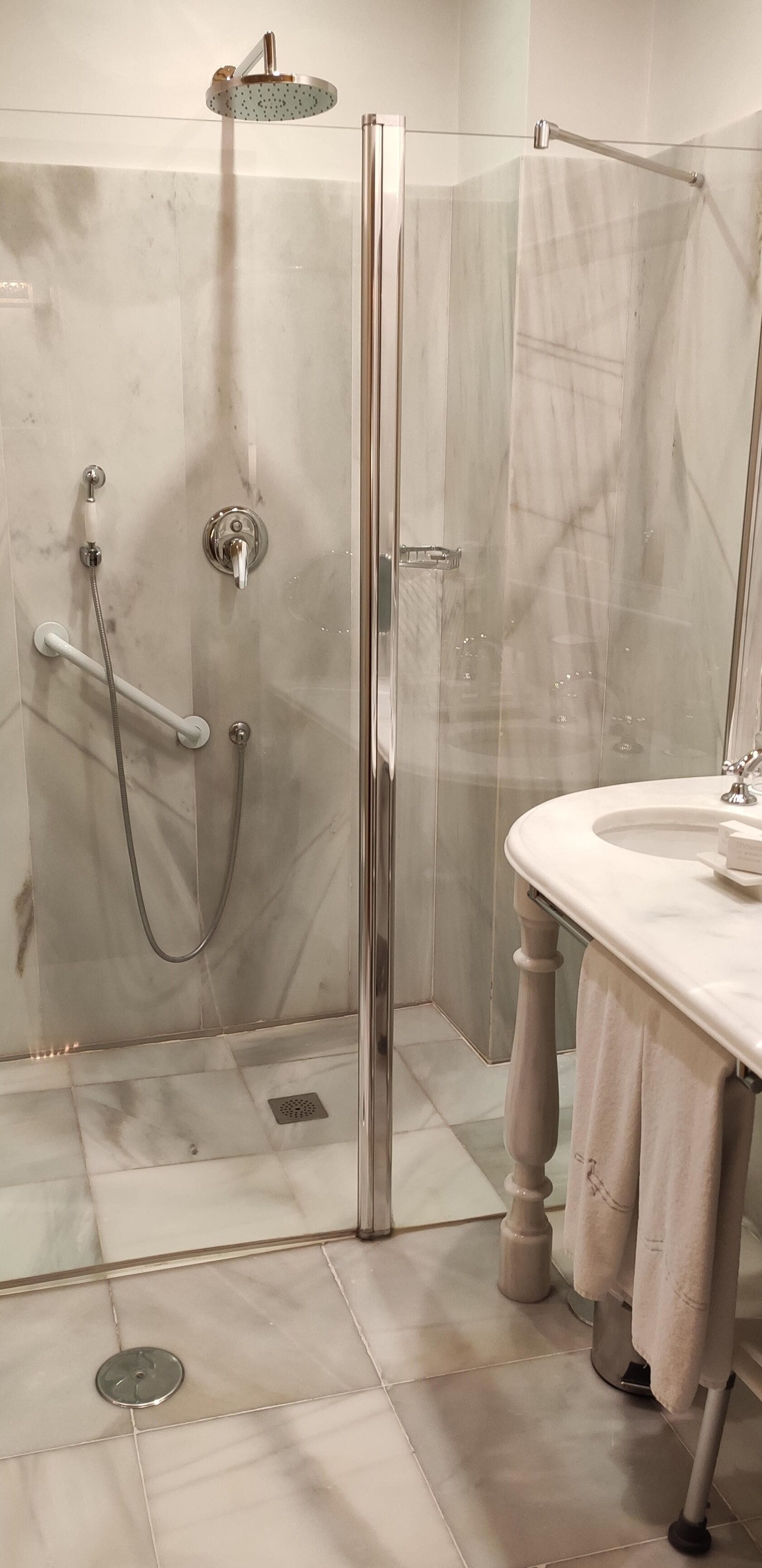 Un bagno moderno con doccia vetrata, pavimento in marmo e un classico lavandino con porta asciugamani.