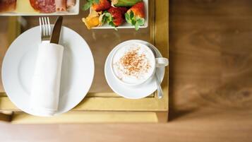 Una mesa de comedor con un plato blanco, una taza de café con canela en polvo y un plato de fresas y verduras.