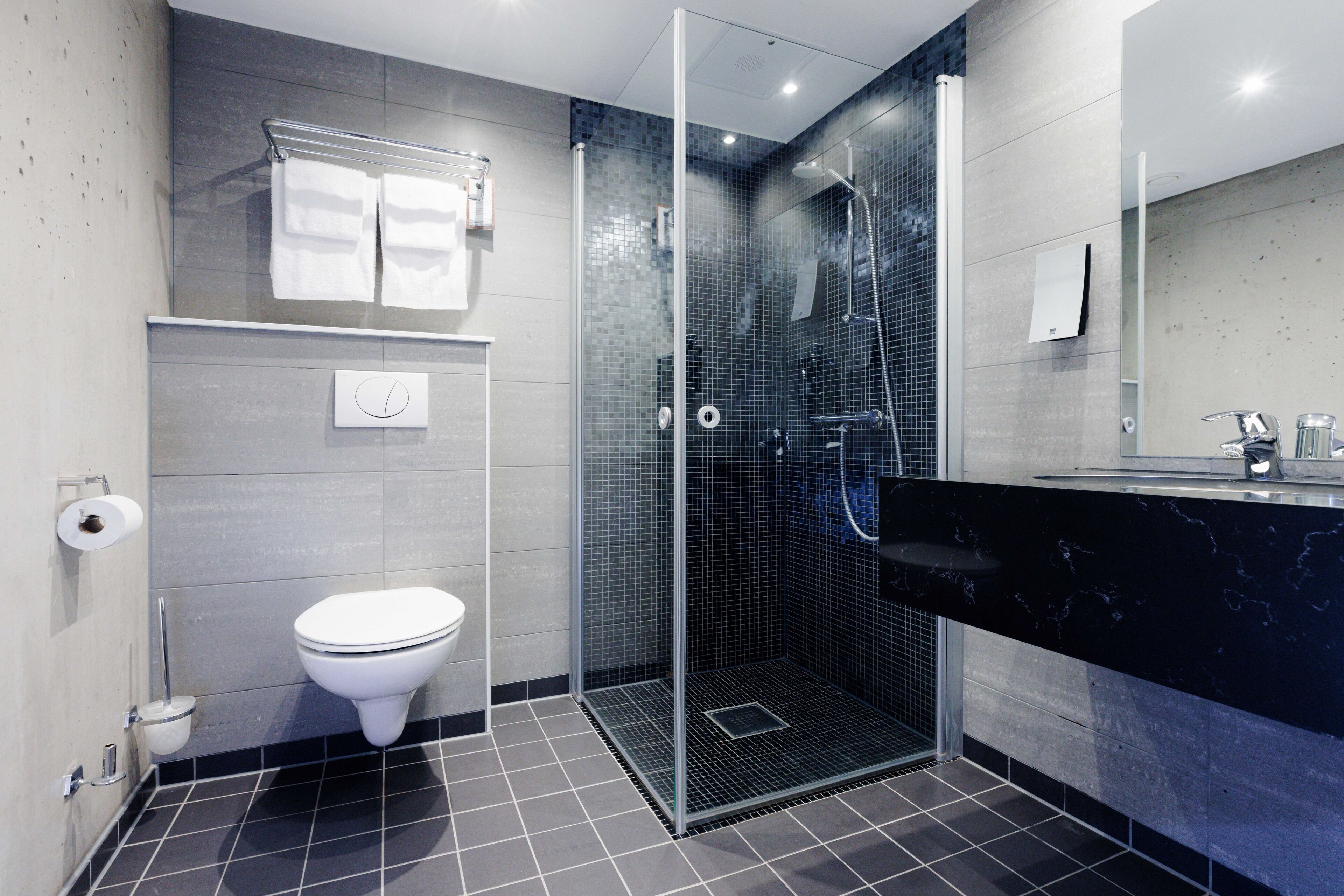 Un baño moderno con ducha de vidrio, inodoro blanco y lavamanos de mármol negro.