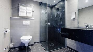 Un baño moderno con ducha de vidrio, inodoro blanco y lavamanos de mármol negro.