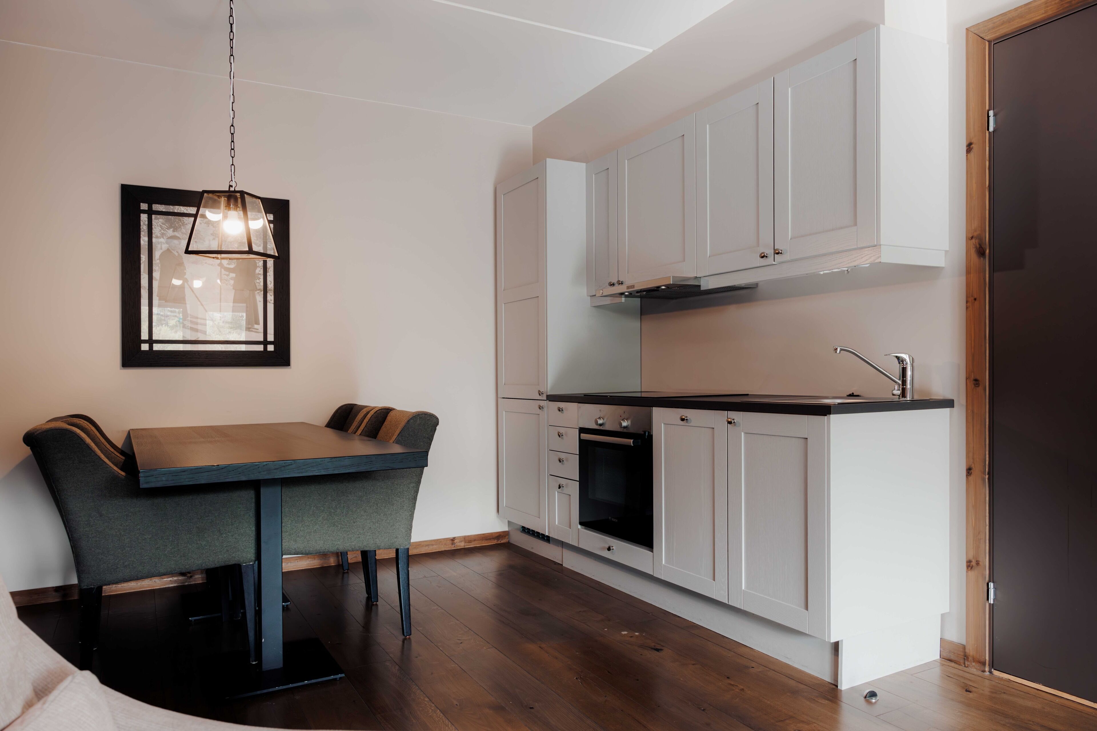 Une cuisine moderne avec des armoires blanches, un plan de travail foncé et un luminaire suspendu.