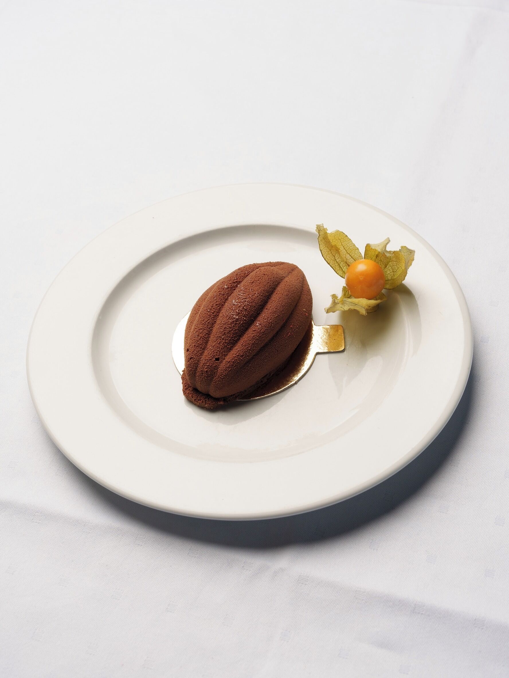 A dessert on a white plate with a leaf and a cherry on top.