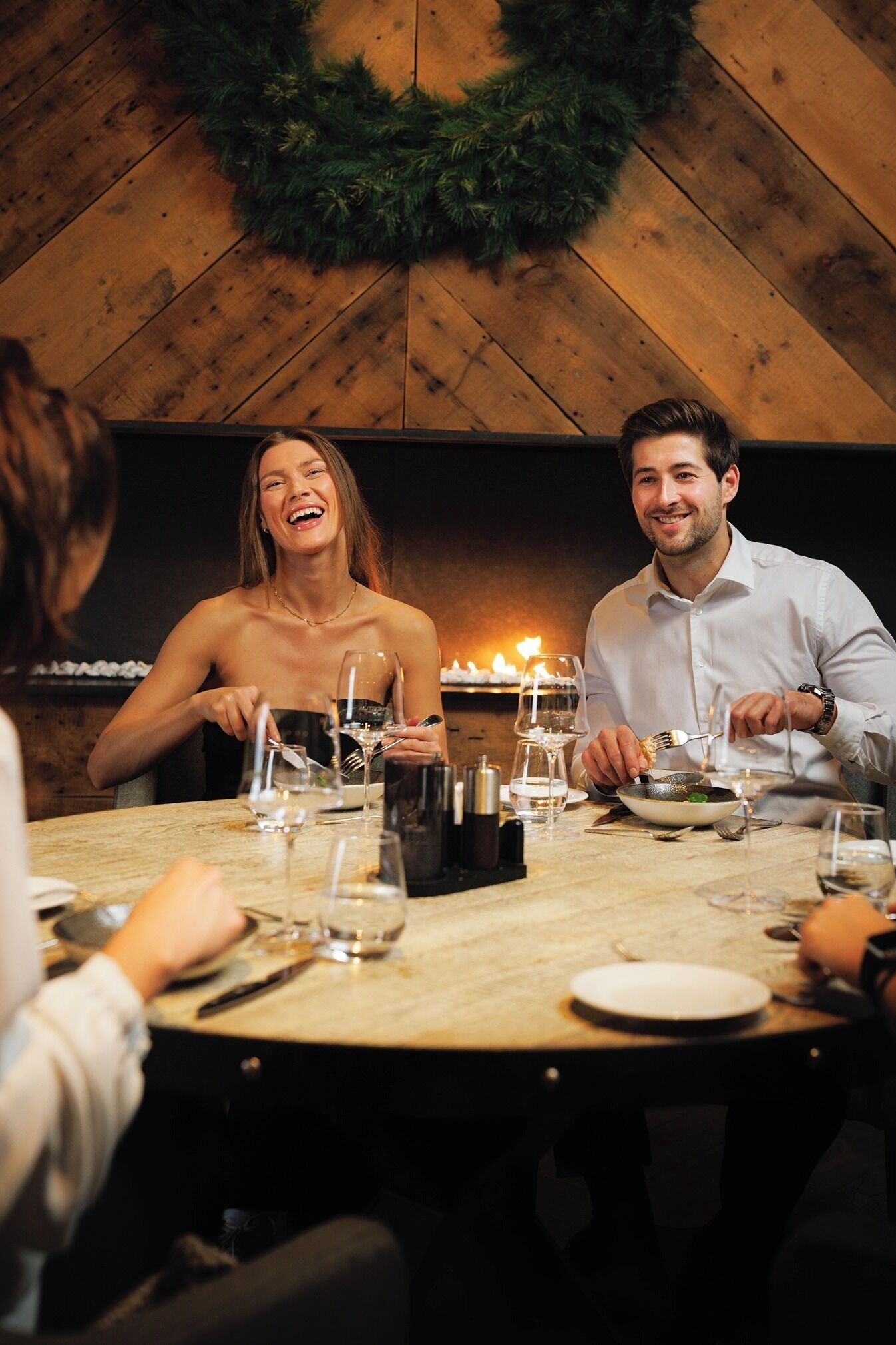 A round dining table with a wooden top, surrounded by chairs, in a room with wooden walls and a fireplace.