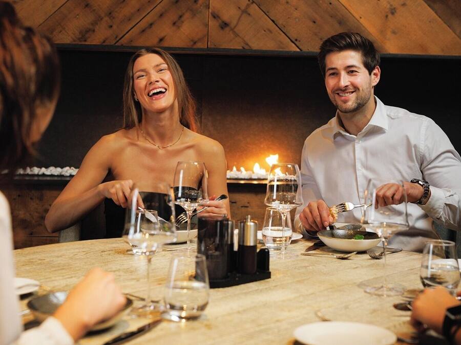 Una mesa de comedor redonda con tapa de madera, rodeada de sillas, en una habitación con paredes de madera y una chimenea.