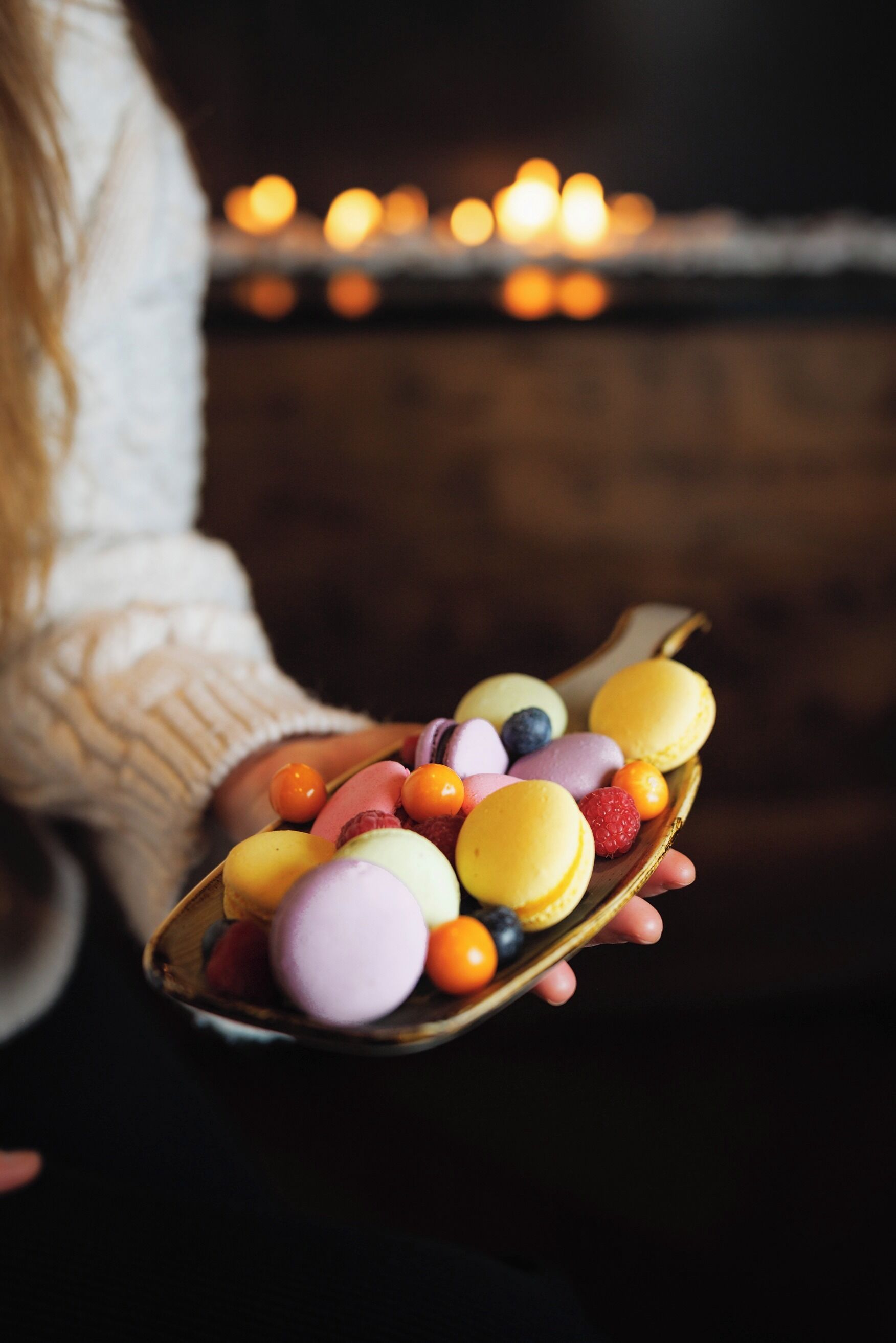 A person holding a spoon with colorful macarons and berries.