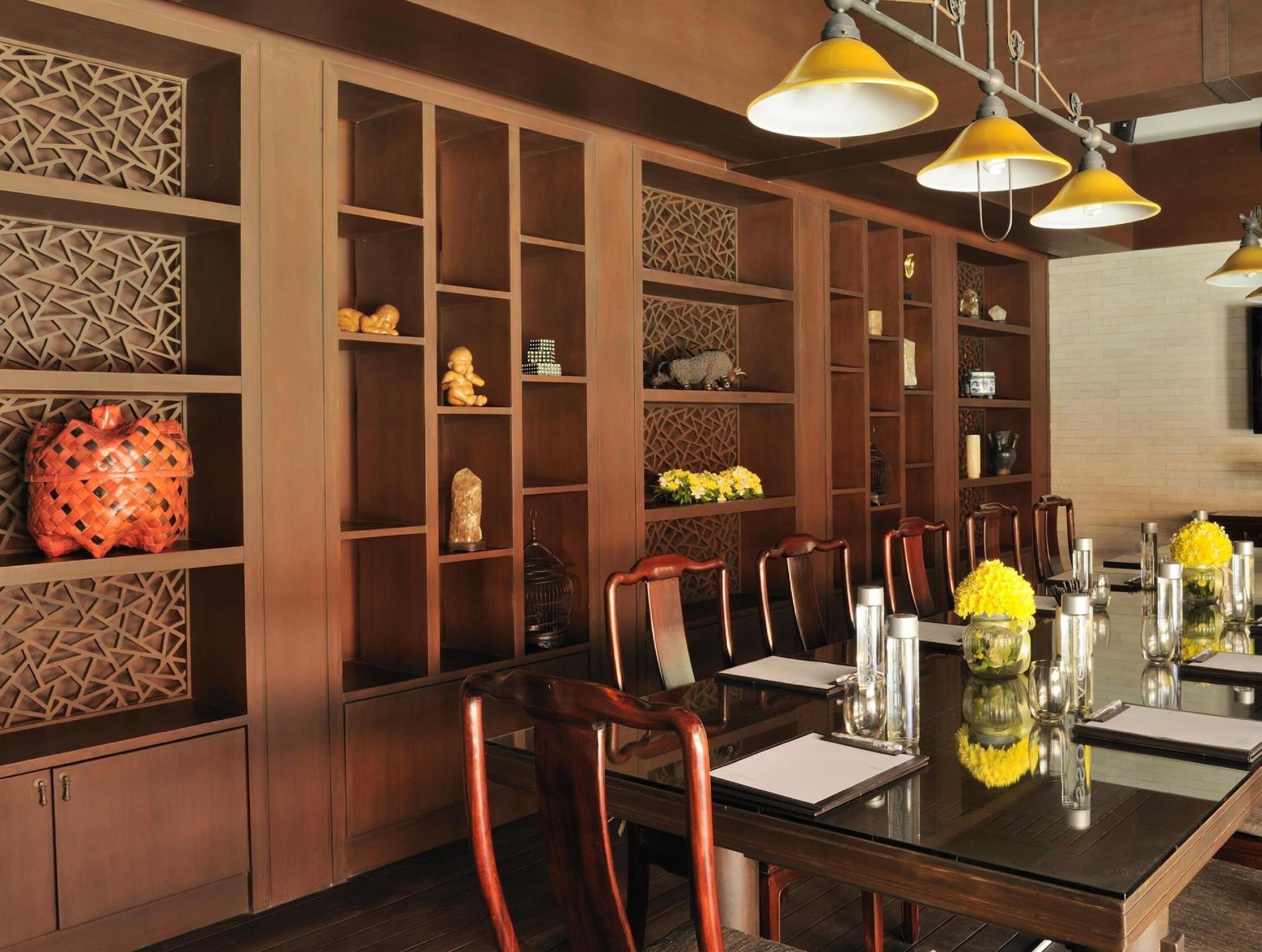 Un comedor con una mesa larga, sillas de madera y objetos decorativos en estanterías.