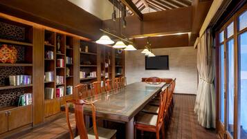 A spacious library with a long wooden table and chairs, surrounded by bookshelves filled with books.