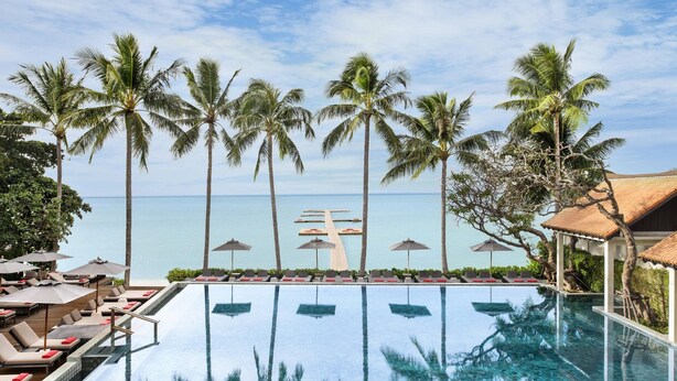 An infinity pool with palm trees and a view of the ocean.