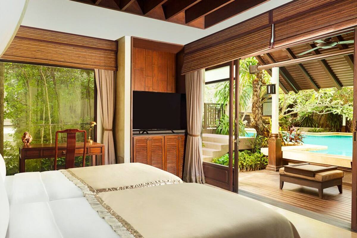 A bedroom with a bed, a TV, a desk, and a view of a pool.