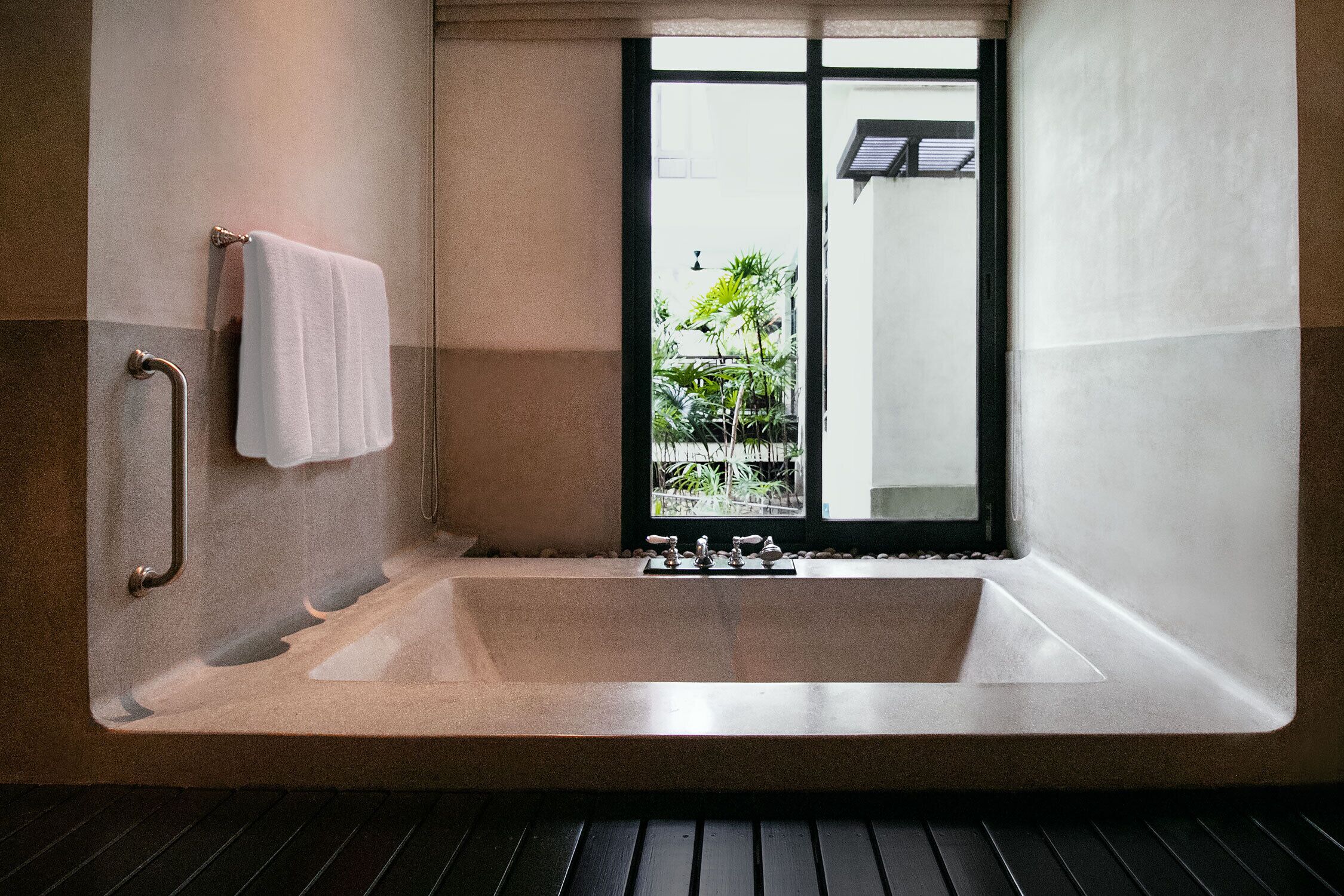 Un baño moderno con una bañera grande, un pasamanos y una ventana con vistas a la vegetación.