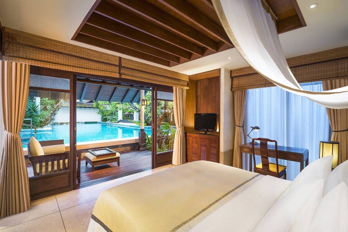 A spacious bedroom with a large bed, a TV, and a view of an outdoor swimming pool.