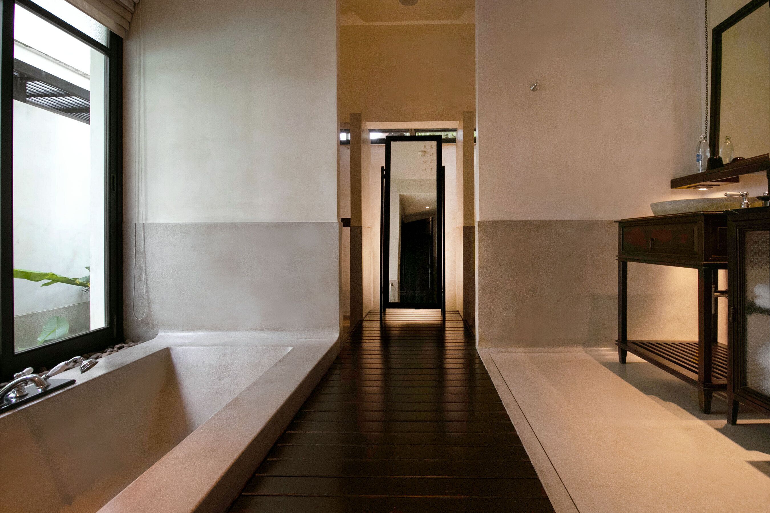 Un pasillo estrecho con una bañera a la izquierda, un banco de madera a la derecha y una puerta al final.