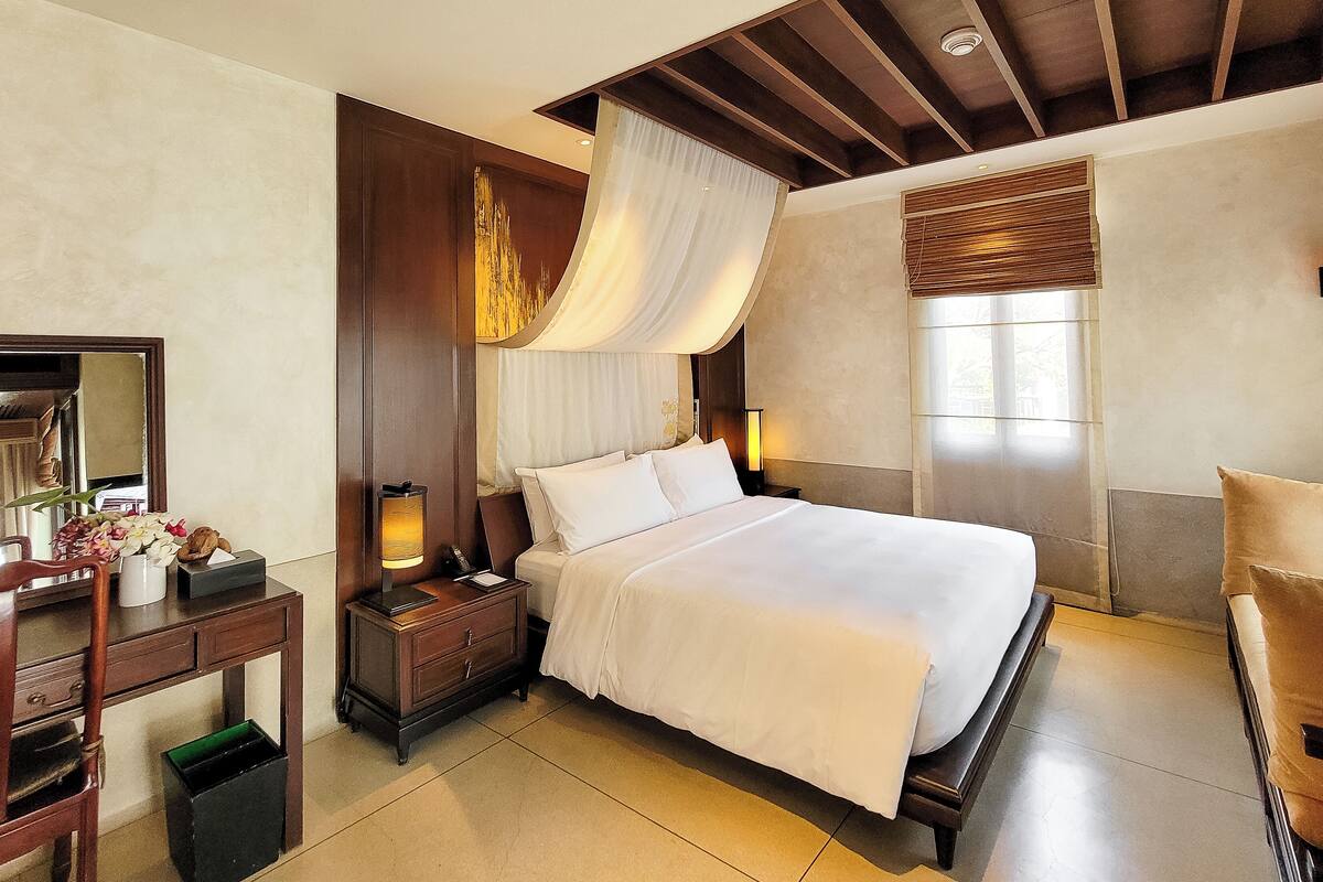 A hotel room with a large bed, a nightstand with a lamp, a wooden desk, and a mirror.