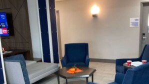 A modern hotel lobby with a sofa, two armchairs, a small table with a pumpkin decoration, and a flat-screen TV mounted on the wall. - Holiday Inn Express Wichita North - Park City by IHG (Wichita)