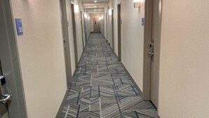 A hotel hallway with a patterned carpet, doors on both sides, and wall-mounted lights. - Holiday Inn Express Wichita North - Park City by IHG (Wichita)