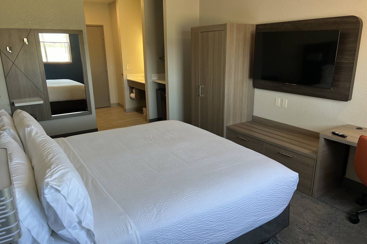 Une chambre d’hôtel avec un grand lit, un téléviseur fixé au mur, un bureau avec une chaise et une armoire.