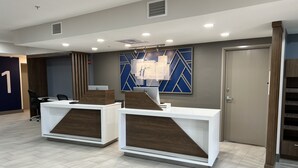 A reception area with two white reception desks, a blue geometric wall decoration, and a door with a number '1' sign. - Holiday Inn Express Wichita North - Park City by IHG (Wichita)