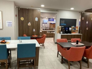 A modern cafe with wooden walls, orange and blue chairs, and a coffee station. - Holiday Inn Express Wichita North - Park City by IHG (Wichita)