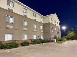 A multi-story hotel building with a flat facade, large windows, and a parking lot with marked spaces.