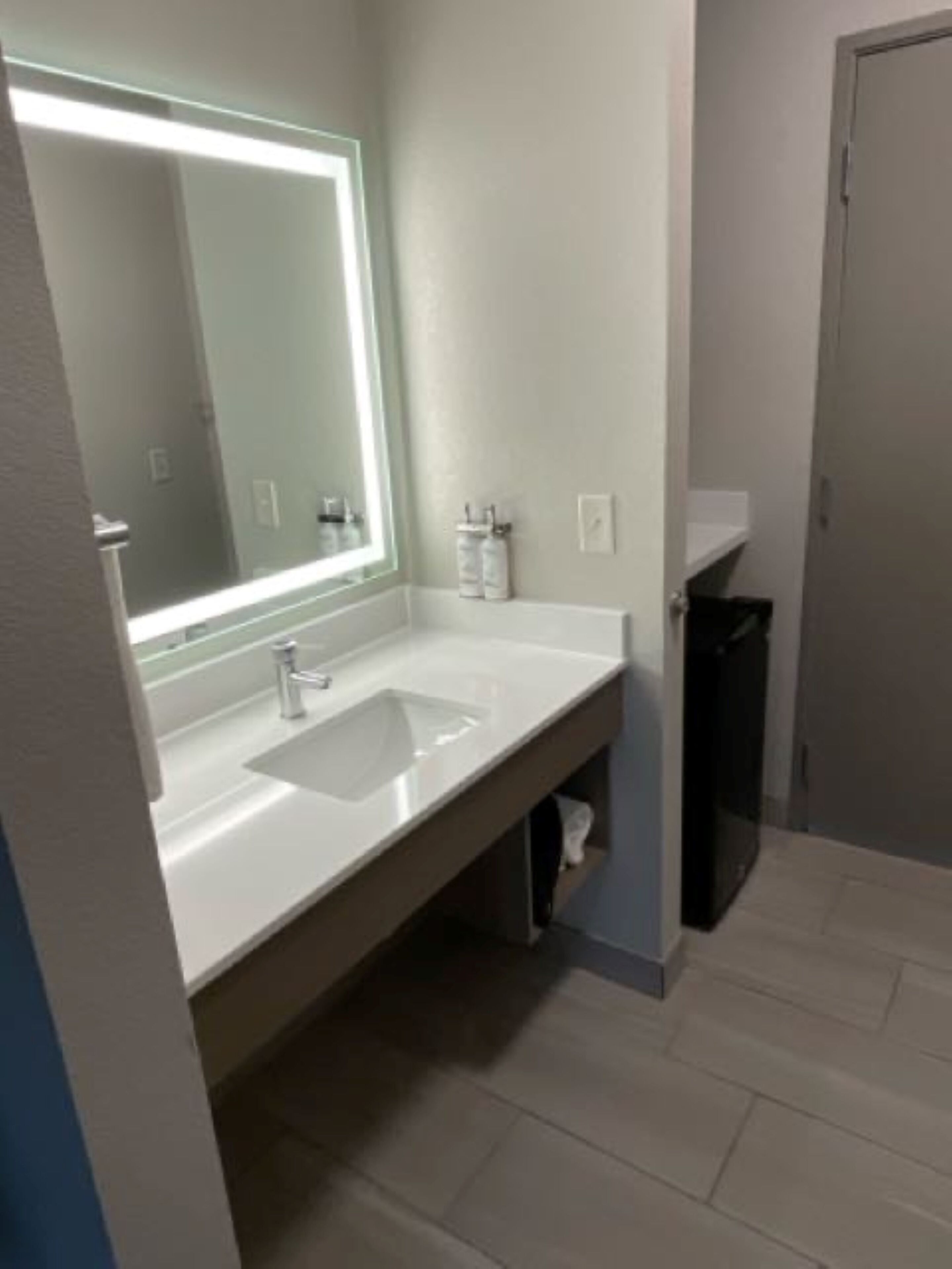 A modern bathroom with a large mirror, two sinks, and a trash bin.