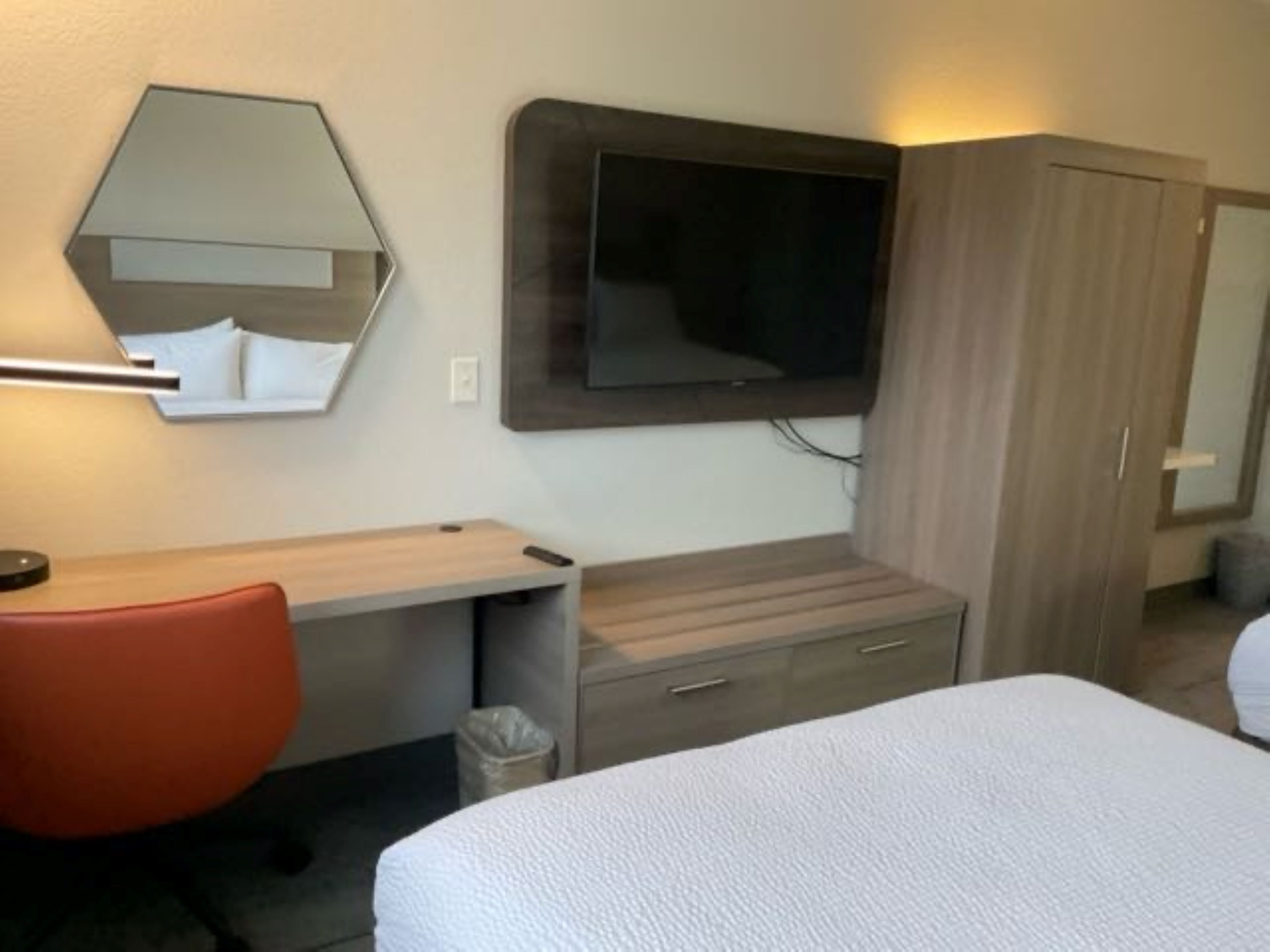 Et hotelværelse med seng, skrivebord med stol, garderobeskab, spejl og tv.