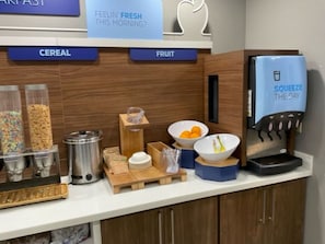 A breakfast station with cereal and fruit options, a coffee machine, and a juice dispenser.