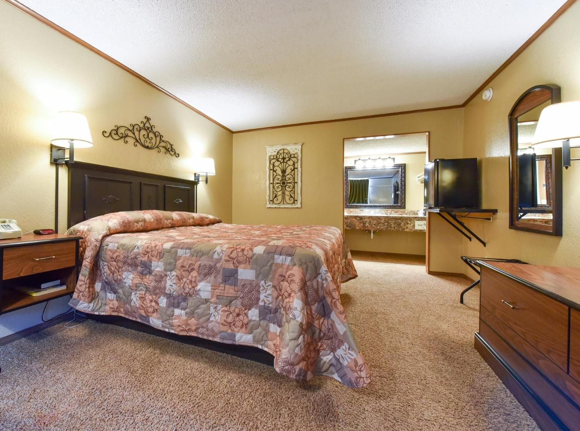 A hotel room with a bed, a desk, a dresser, a television, and a bathroom mirror.