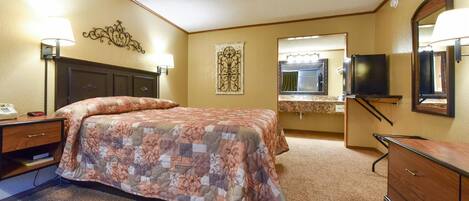 A hotel room with a bed, a desk, a dresser, a television, and a bathroom mirror.