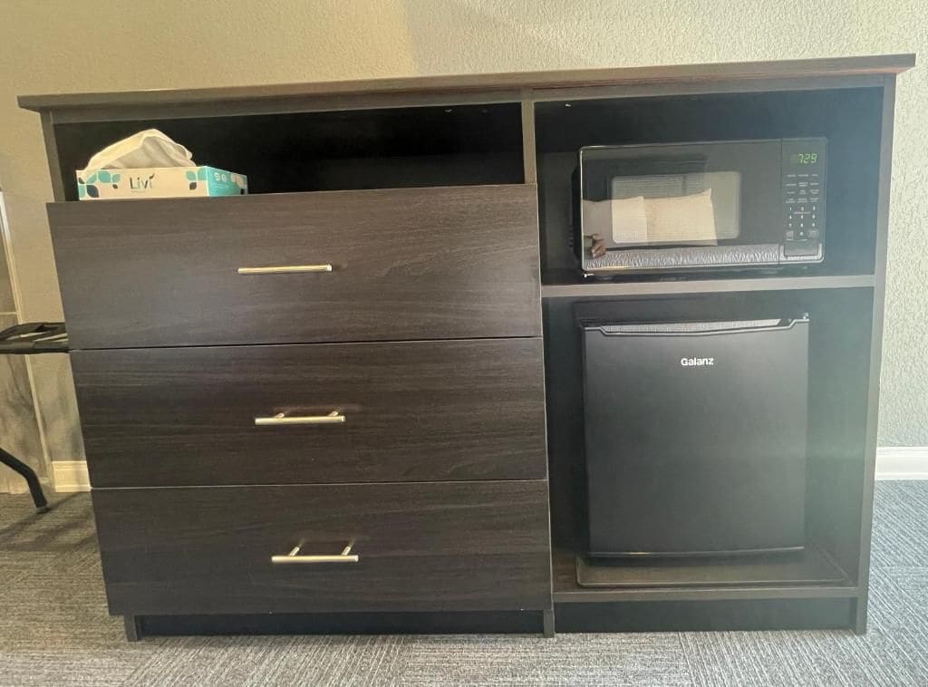 A dark wooden cabinet with drawers and a microwave on top.