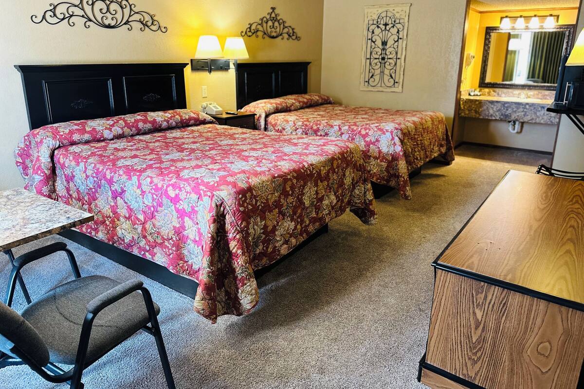 A hotel room with two beds, a desk, a chair, a telephone, and a bathroom mirror.