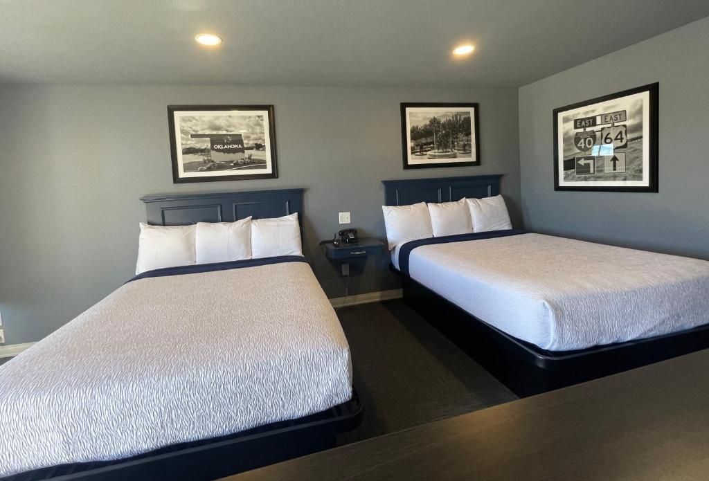 A hotel room with two beds, a nightstand, and framed pictures on the wall.
