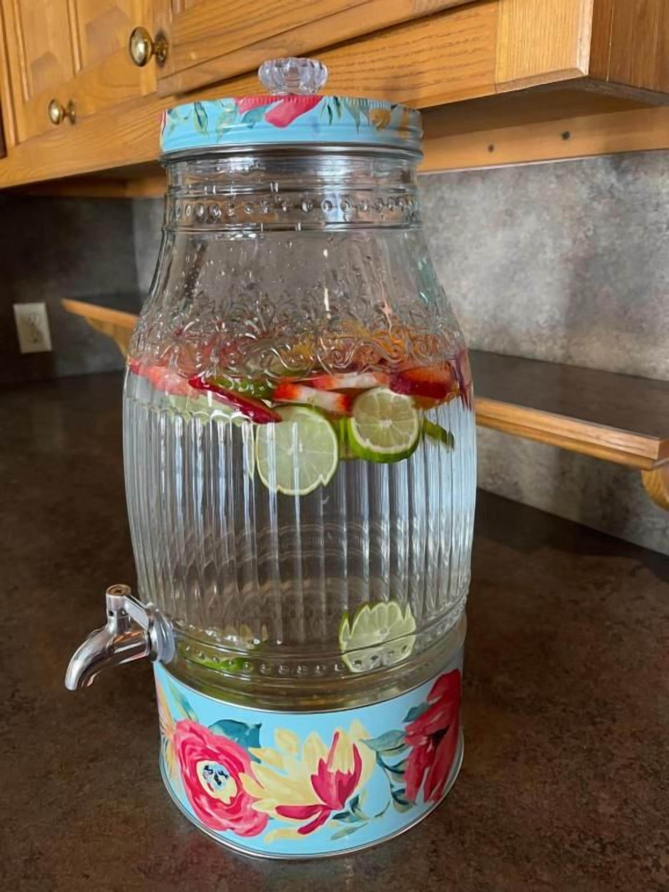 A clear glass container with a floral design, containing sliced fruits and a metal tap.