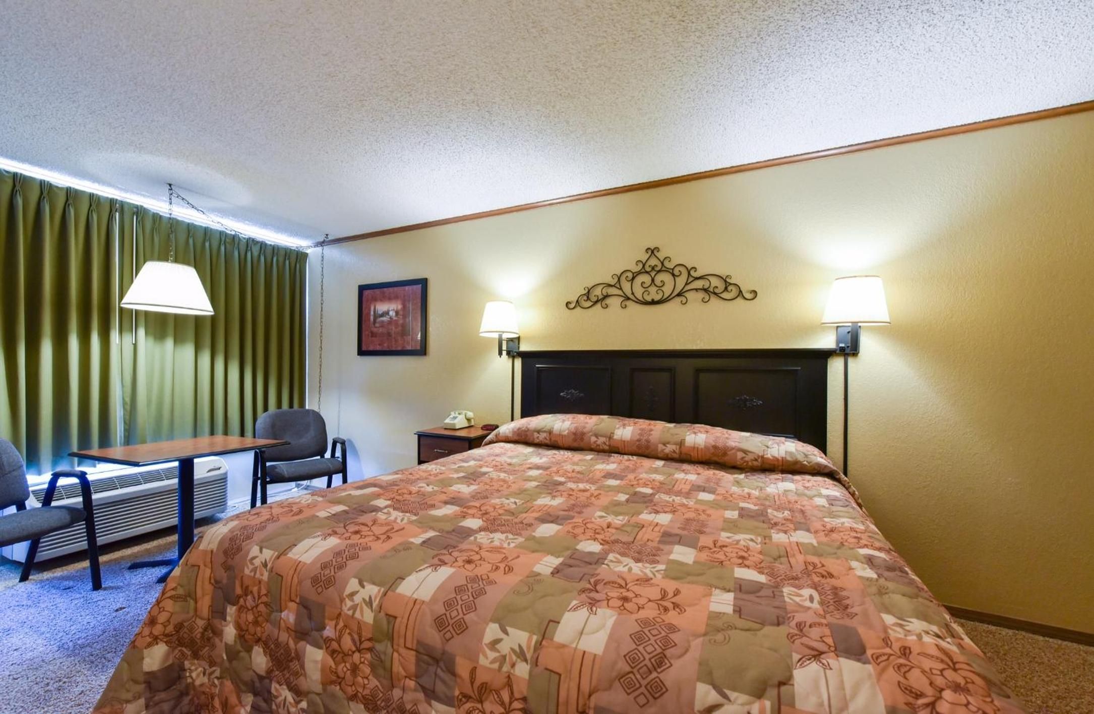 A hotel room with a bed, a desk, a chair, a nightstand, and a lamp.