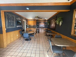 A restaurant with a high ceiling, wooden paneling, and a tiled floor. There are multiple tables and chairs, a ceiling fan, and wall-mounted decorations.