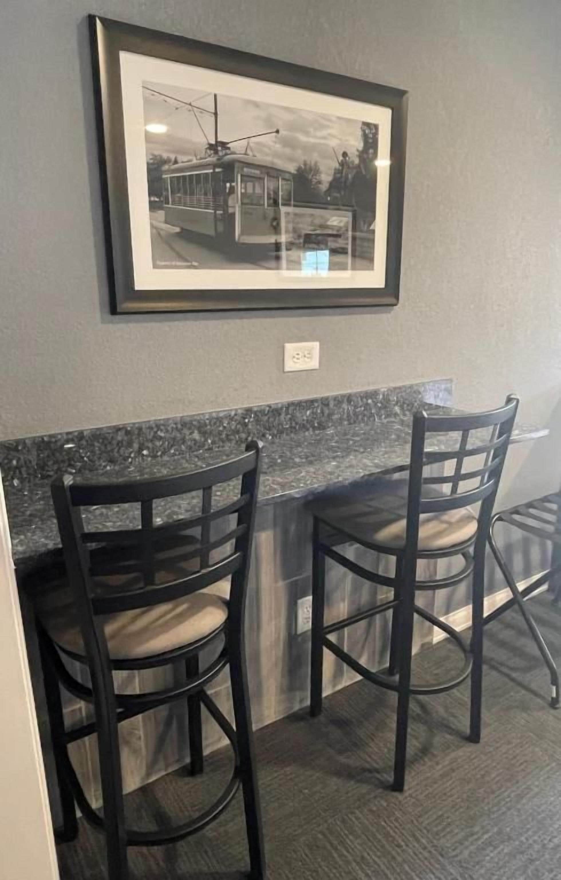 A framed black and white photo of a tram on a wall, two dark chairs with light cushions, and a granite countertop.