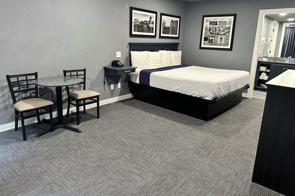 A bedroom with a bed, a desk, and chairs. There are framed pictures on the wall.
