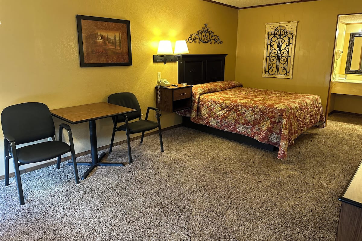 A hotel room with a bed, a desk, two chairs, a lamp, a telephone, and a picture on the wall.