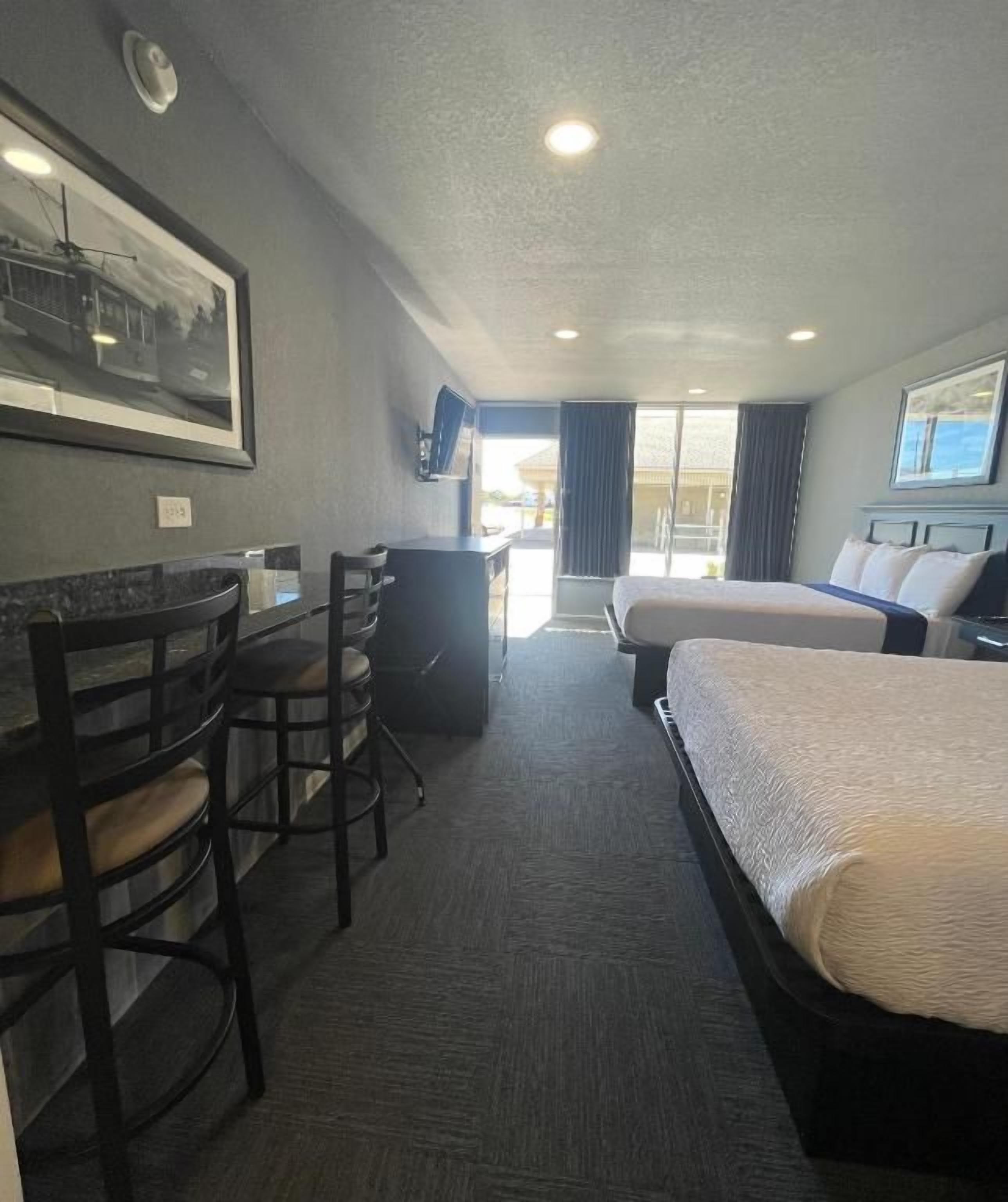 Habitación de hotel con cama, escritorio y silla. Cuenta con una ventana con cortinas y un televisor montado en la pared.