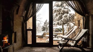 Una habitación acogedora con chimenea, un sillón y vistas a un paisaje nevado a través de un ventanal.