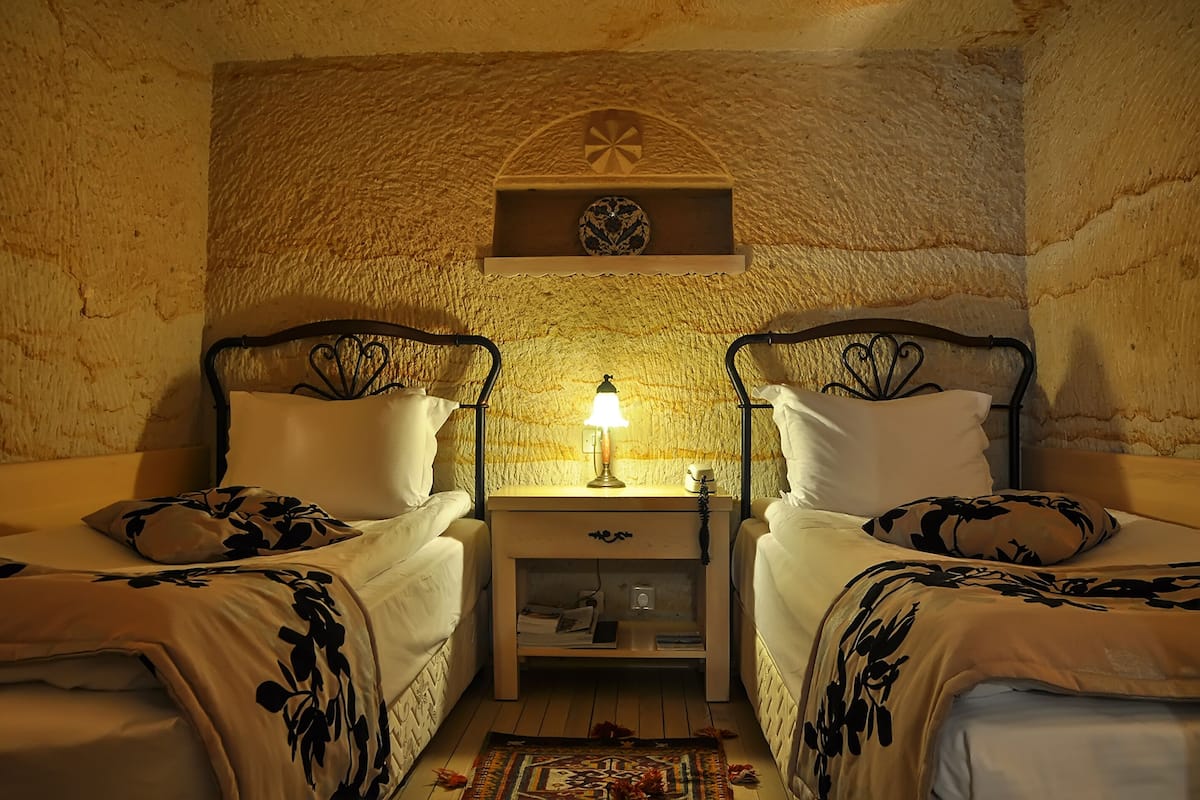 A cozy room with two beds, a nightstand with a lamp, and a decorative shelf above the beds.