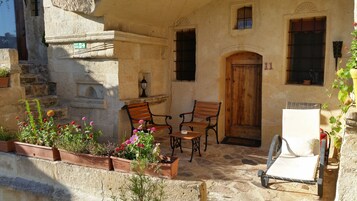 Un edificio de piedra con puerta de madera, dos bancos y macetas con plantas.