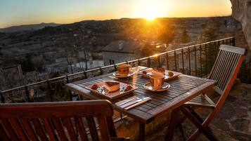 Mesa de madera para dos personas con un postre, una taza y un platito, con vistas a un paisaje montañoso al atardecer.