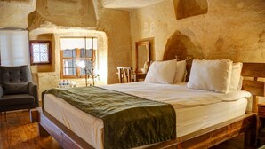 Una cama de madera con una manta verde, una mesita de noche de madera, una silla y una ventana con vistas al exterior.