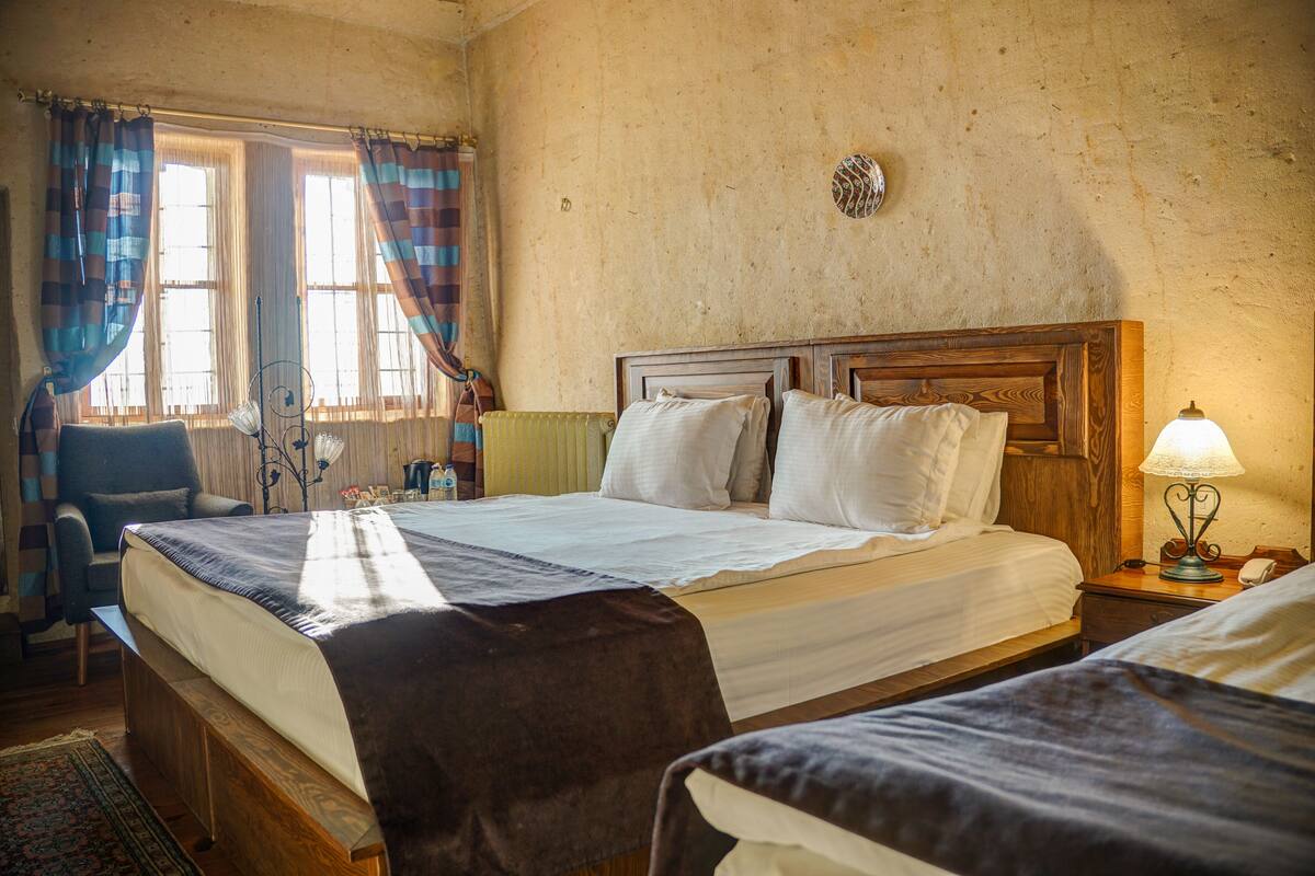 A room with two beds, a chair, a lamp, and a window with curtains.