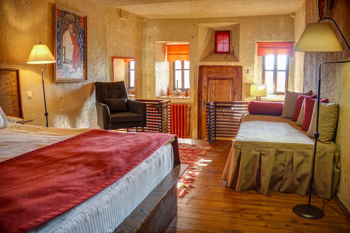 A room with two beds, a chair, a radiator, and a painting on the wall.