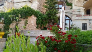 Un edificio de piedra con un balcón, una estatua y flores rojas en primer plano.