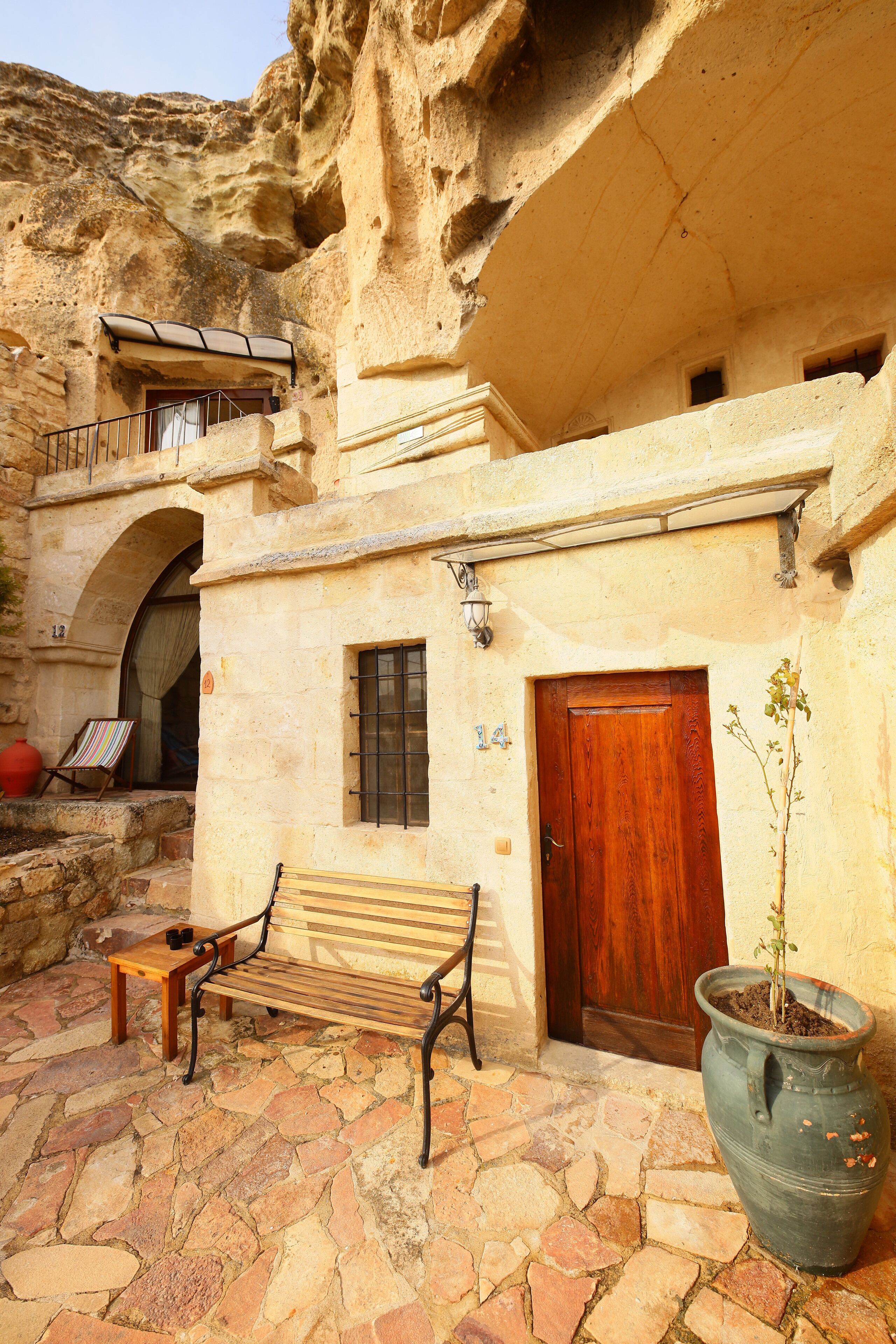 A stone building with a wooden door, a bench, a potted plant, and a small table.