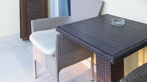 Un balcón con mobiliario de mimbre, una mesa y una ventana con persianas.