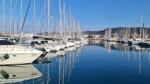 Un puerto deportivo con numerosas embarcaciones amarradas en aguas tranquilas, rodeado de colinas al fondo.