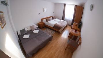 A hotel room with two beds, a wooden floor, a small round table, and a wardrobe.